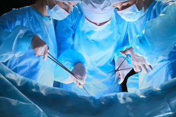 Fototapeta na wymiar Group of surgeons at work in operating theater toned in blue