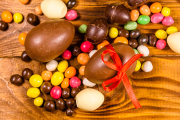 Chocolate easter eggs and multicolored candies on wooden table. Top view