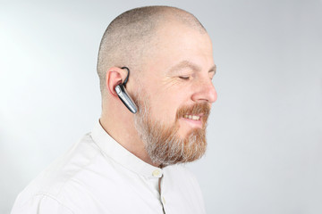 Obraz premium Bearded man in a light shirt with a Bluetooth in his ear.