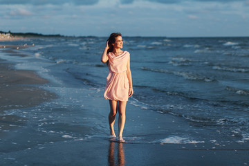 Fototapeta na wymiar beautiful girl in pink dress strolls along the seashore in the evening