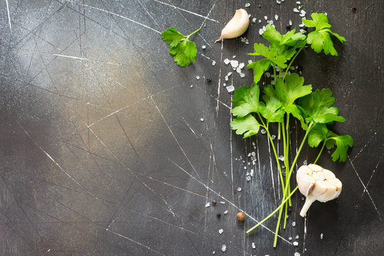 Ingredients for cooking on a dark stone table - parsley, garlic and spices. Copy space, top view flat lay background.