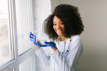 Young beautiful African American girl doctor in a white coat with a stethoscope. sitting near the...