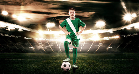 Kid - soccer player. Boy forward in football sportswear on stadium with ball. Sport concept.