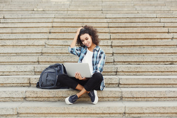 Fototapeta na wymiar Smiling student sitting on stairs using laptop