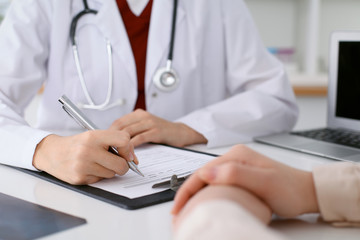 Fototapeta premium Close up of a female doctor filling up an application form while consulting patient