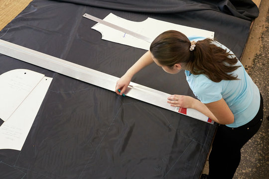 The Cutter Girl Works At A Large Table, Marking A Fabric With A Ruler For Further Sewing Of Working Clothes.