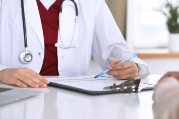 Close up of a female doctor filling up  an application form while consulting patient