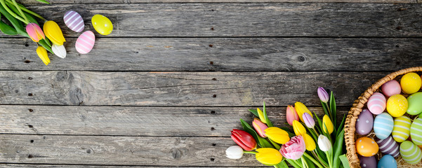 above top view of multi colored painted easter eggs with springtime tulip bouquet flowers on a old wood plank