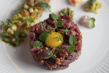 Beef tartare with a quail egg and green mint and sauteed vegetables on a white plate