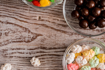Frame of colorful bright assorted candy in bowls and jars, candy canes and rainbow colored spiral lollipops on black with scattered candy hearts and jellybeans around a central copy space on slate