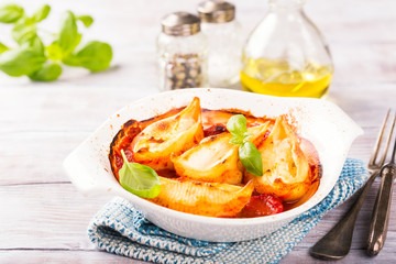 Italian pasta Conchiglioni Rigati stuffed with three sorts of cheese and and baked in tomato sauce in white wooden plate on rustic wooden background. Healthy food concept.