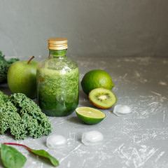 Healthy green smoothie with ingredients and ice cubes on gray background