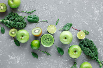 Healthy green smoothie with ripe green fruits, kale and spinach on gray background, top view