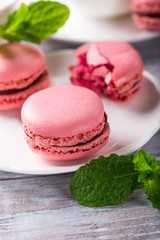 French raspberry macaroons with mint leaves on old white wooden background. Holidays food concept.