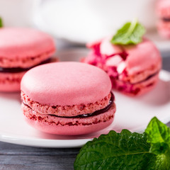 French raspberry macaroons with mint leaves on old white wooden background. Holidays food concept.