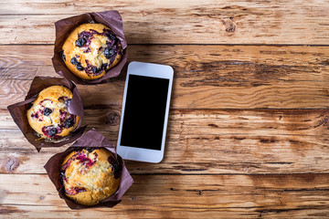 Fresh muffins with berries and smartphone on a wooden table top view.