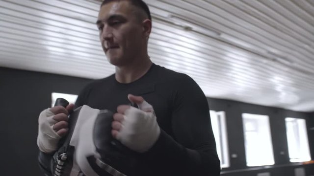 Fit young woman in boxing gloves throwing kicks and punches at her sports instructor during kickboxing workout at the gym, medium shot