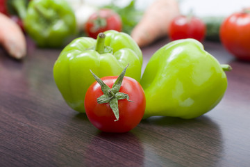 Red tomatoes and green peppers on a table on the background of vegetables. Fresh tomatoes and peppers on a wooden brown table..