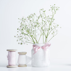 Soft composition with white gypsophila, silk ribbon on wooden spool. White background