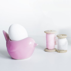 White Easter Egg in pink egg stand with silk ribbon on wooden spool