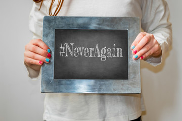 Young girl holding up blackboard with text #neveragain