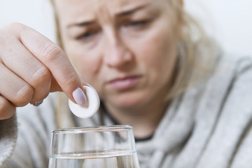 Sick woman with high fever. Young woman throws a tablet into a glass of water.