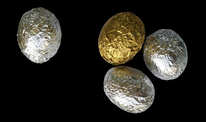 One golden and three silver eggs on a black background.Eggs covered with crumpled foil