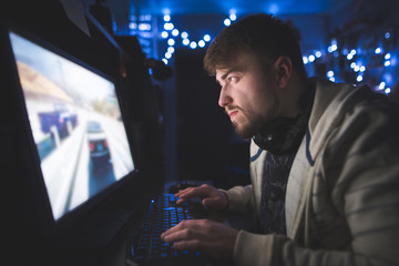 Portrait of a focused gamer while playing a home at a computer. A man with a beard and headphones plays computer games in his room. Cozy gaming room.
