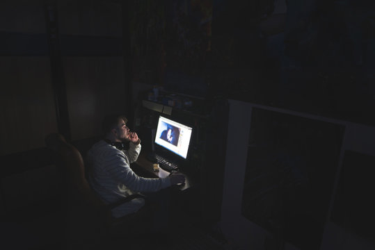 A man is sitting at home in a dark room and uses the internet on a  computer. Work at a computer at home. Night snack. Stock Photo | Adobe Stock