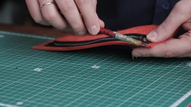 Leathersmith is applying glue on a leather parts of the zipper with a special brush. He works at the table in the workshop.
