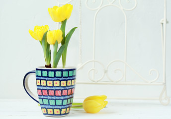 Yellow tulips with bulbs in a multicolored ceramic cup on a light background. Selective focus.