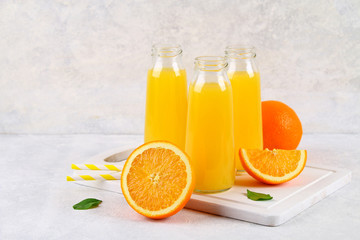 Fototapeta na wymiar Glass bottles with fresh orange juice with orange slices and yellow tubes on a light gray table.