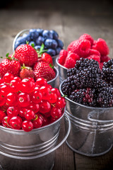 Berries arrangement closeup assortment in siver color tin cans on rustic wooden table in studio. Red currant, blackberries, raspberries, strawberries, blueberries.