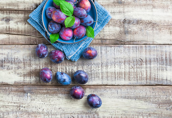 Plums fresh overhead colorful arrangement with green leaves on blue plate and cloth on white rustic wooden table in studio