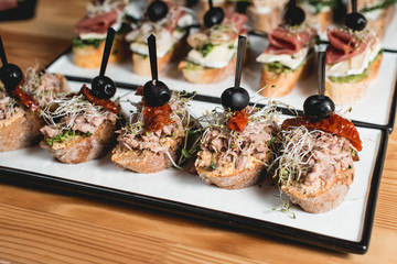 tasty pinchos with tuna, dried tomatoes, olive and pesto sauce, traditional spanish snack, served on a white plate
