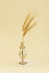 glass vase with a few ripe spikelets of rye Secale cereale on a white round knitted napkin on a...