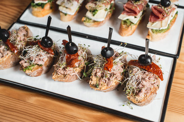 tasty pinchos with tuna, dried tomatoes, olive and pesto sauce, traditional spanish snack, served on a white plate