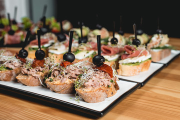 tasty pinchos with tuna, chorizos, salmon, egg, dried tomatoes, avocado, salmon, bacon, Hamon, Brie Cheese, Olives and Pesto Sauce, traditional spanish snack