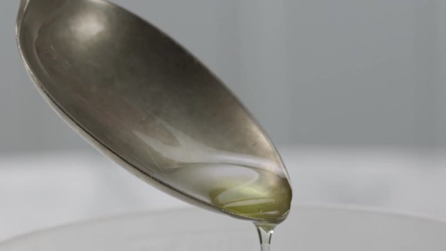 Oil pouring into a vintage tablespoon in the kitchen, shallow focus, slow motion