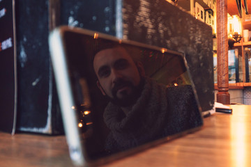 A young man with a beard is reflected in the brilliant reflection of a large screen smartphone