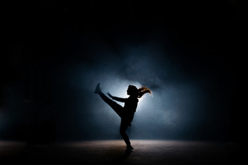 young dancer with long hair raising up her leg on dark stage. flexible girl. dancing moves.extended legs