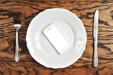 White smartphone with big screen on the plate with knife and fork on the wooden background