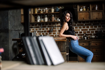 Obraz na płótnie Canvas Beautiful brunette in the kitchen, modern housewife, fashion, wooden brown furniture, dressed in blue jeans and a blue shirt
