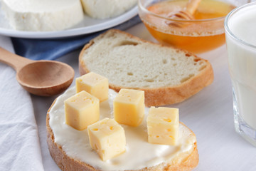 Cheese and honey on a white plate, kefir and sandwich with soft cheese, minimalism, honey and a piece of bread on the blue napkin, French breakfast on a white background, American cuisine