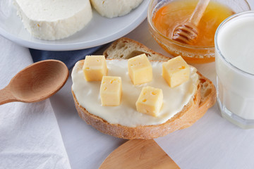 Cheese and honey on a white plate, kefir and sandwich with soft cheese, minimalism, honey and a piece of bread on the blue napkin, French breakfast on a white background, American cuisine