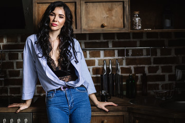 Beautiful brunette in the kitchen, modern housewife, fashion, wooden brown furniture, dressed in blue jeans and a blue shirt