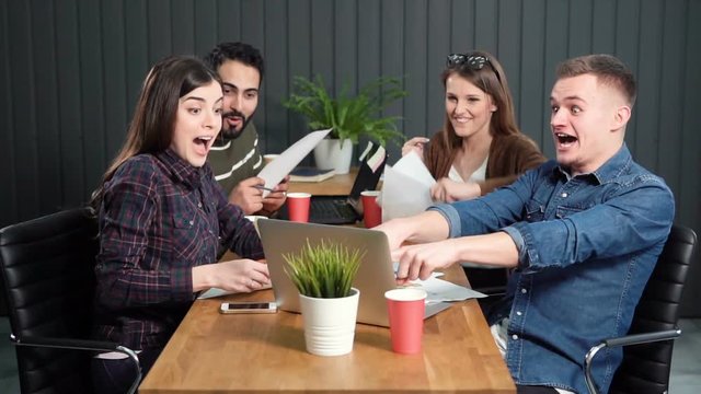 Thrilling reaction of it team to great success, four young workers feeling really happy, indoor slowmotion in small modern office