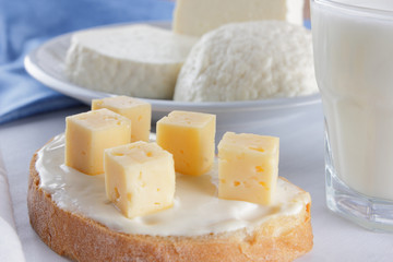 Cheese, dairy assortment on a white background, sandwich with soft cheese on a blue napkin, wooden background, wooden cutlery, white cheese on a white plate, kefir in a glass, art