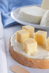 Cheese, dairy assortment on a white background, sandwich with soft cheese on a blue napkin, wooden background, wooden cutlery, white cheese on a white plate, kefir in a glass, art