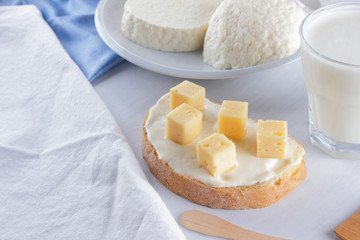 Cheese, dairy assortment on a white background, sandwich with soft cheese on a blue napkin, wooden background, wooden cutlery, white cheese on a white plate, kefir in a glass, art